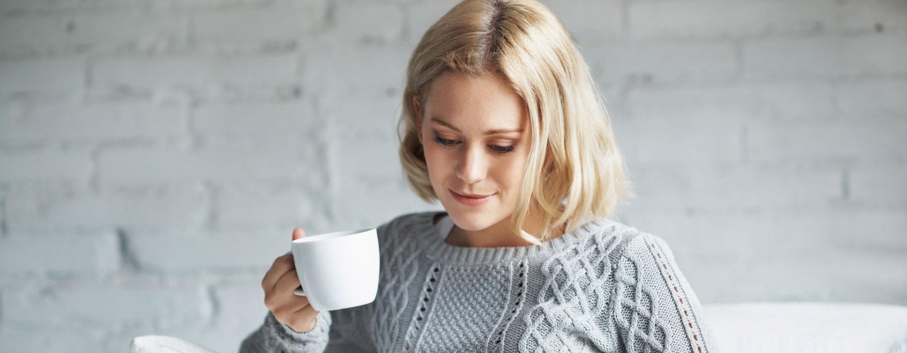 a woman sits on a couch with a cup of coffee and looks at her tablet